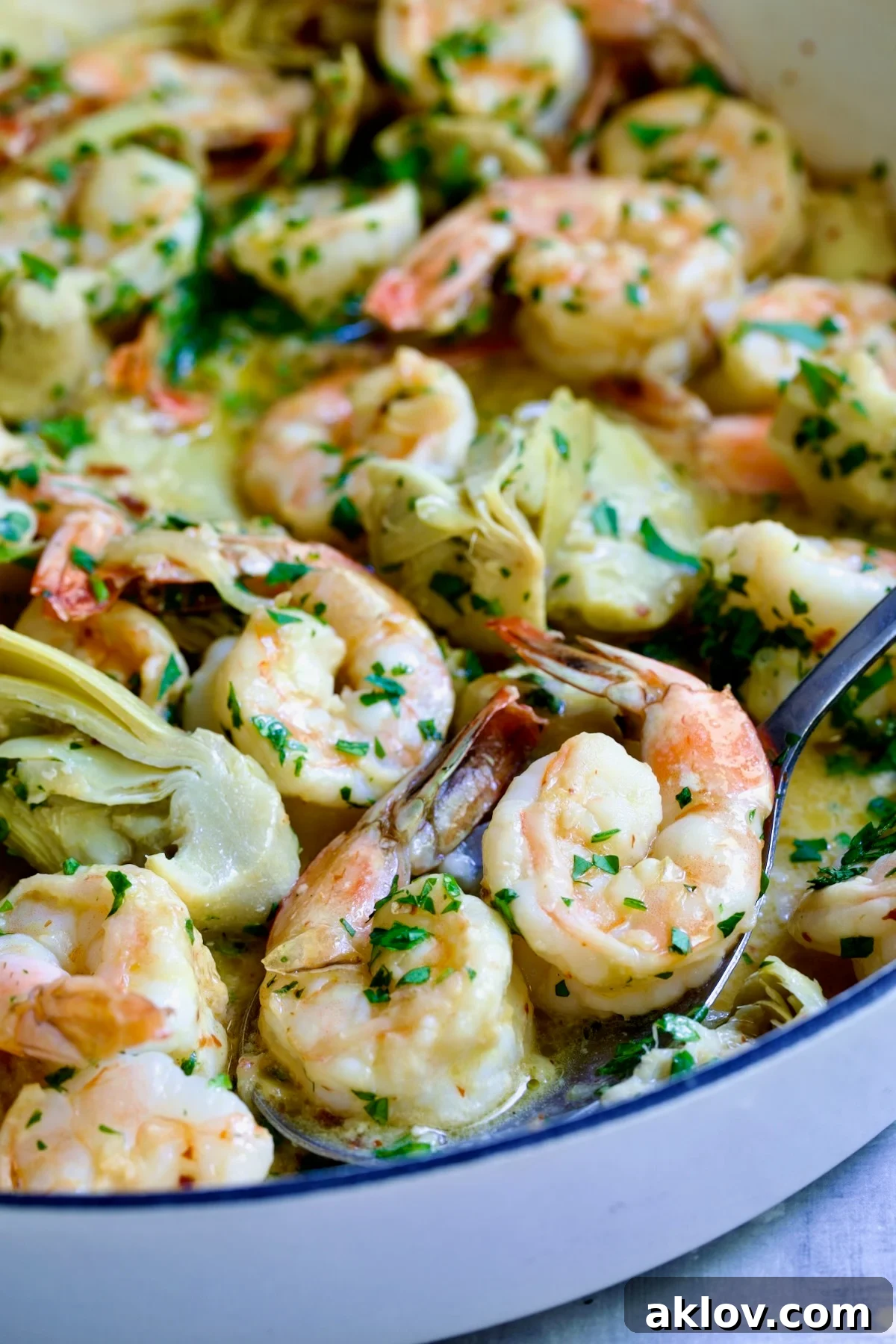 Shrimp Scampi with Artichokes in white enamel cast iron pan with serving spoon scooping two shrimp up.