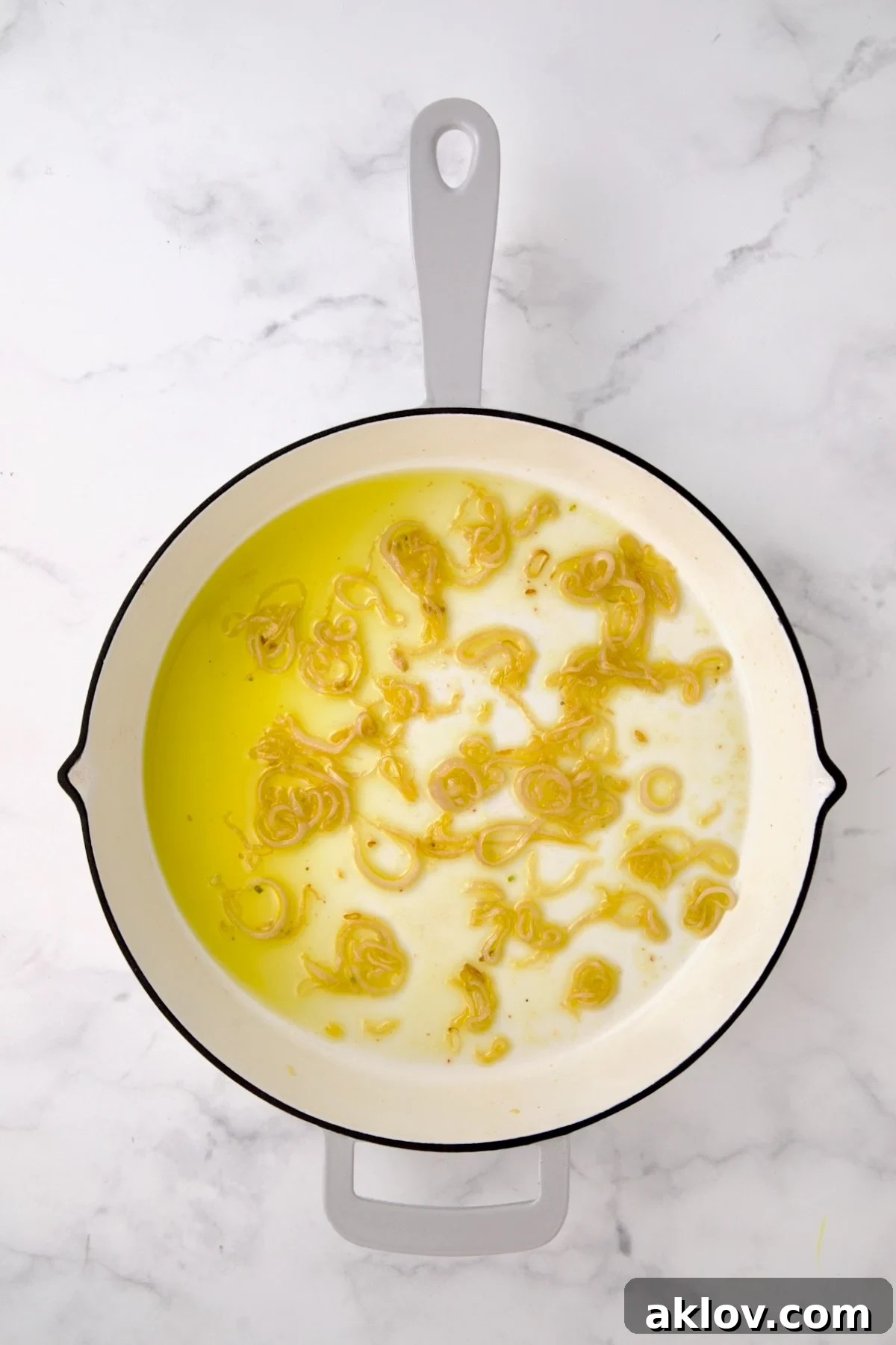 Gently softened shallots cooking in golden olive oil in a white enamel cast iron pan.