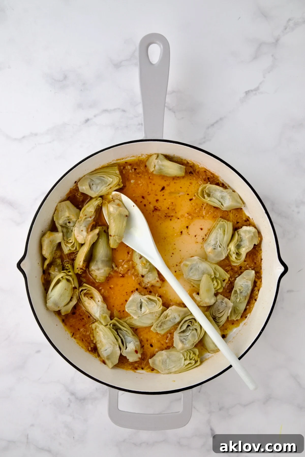 Artichokes added to wine, lemon and shallots in white enamel cast iron pan.