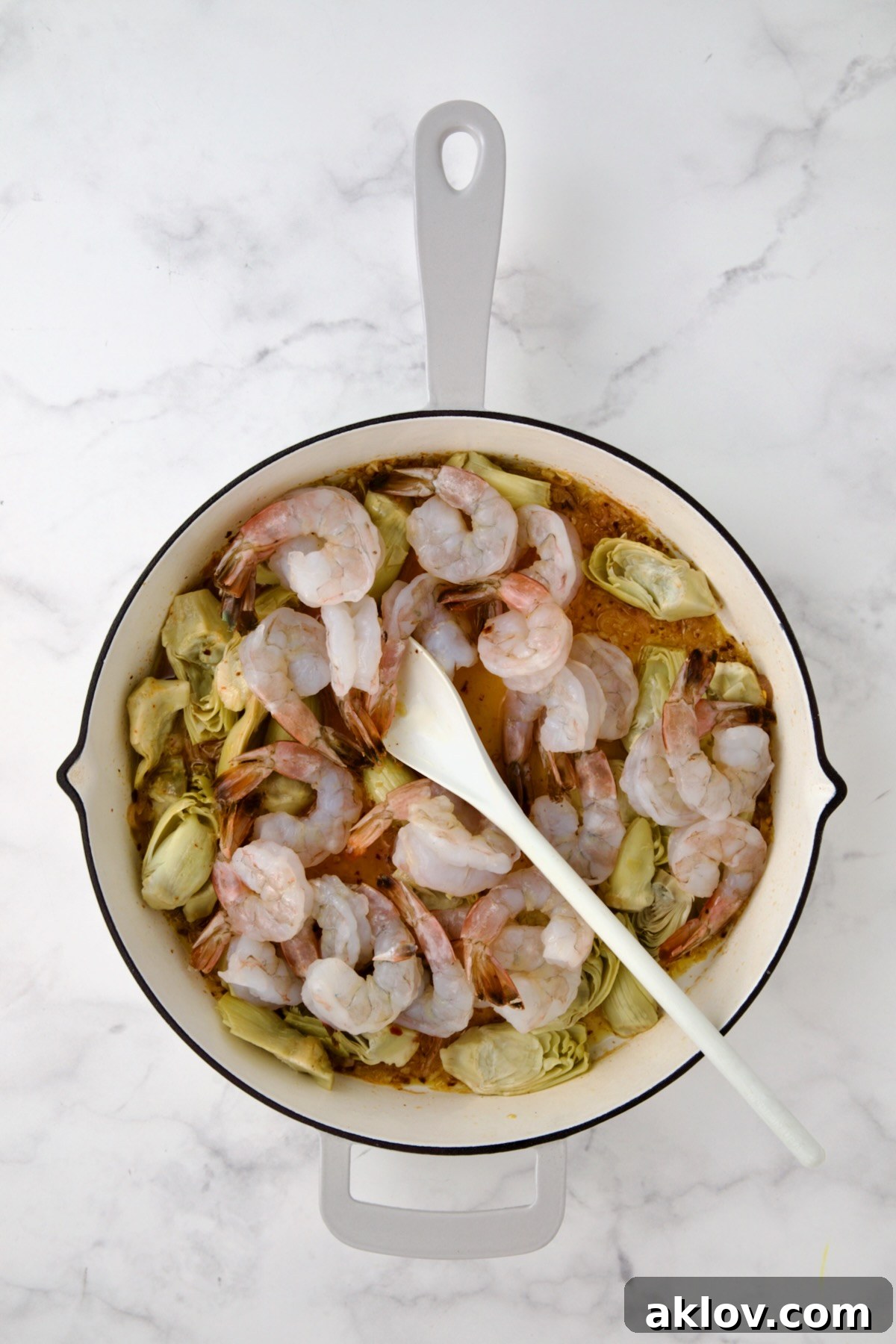 Shrimp turning pink as they cook gently alongside the artichokes in the savory scampi sauce.