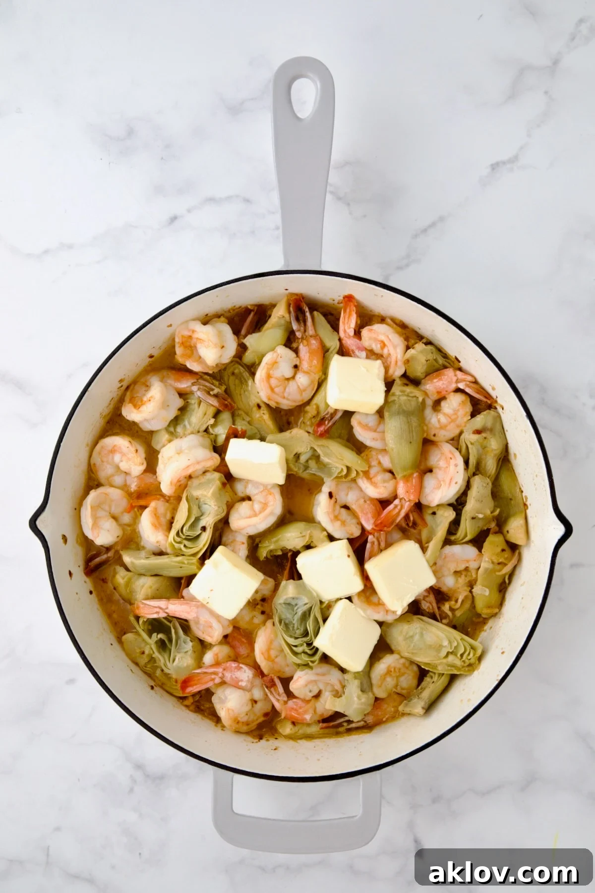 Butter added cooked shrimp and artichokes in white enamel cast iron pan.