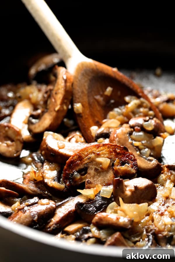 Sliced cremini mushrooms being sautéed in a pan with a wooden spoon, forming the base of the Marsala sauce.