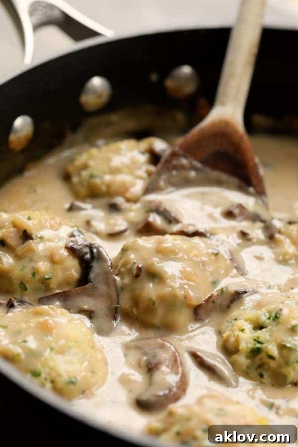 Delicious chicken meatballs simmering in a rich Marsala wine sauce with mushrooms, stirred with a wooden spoon.