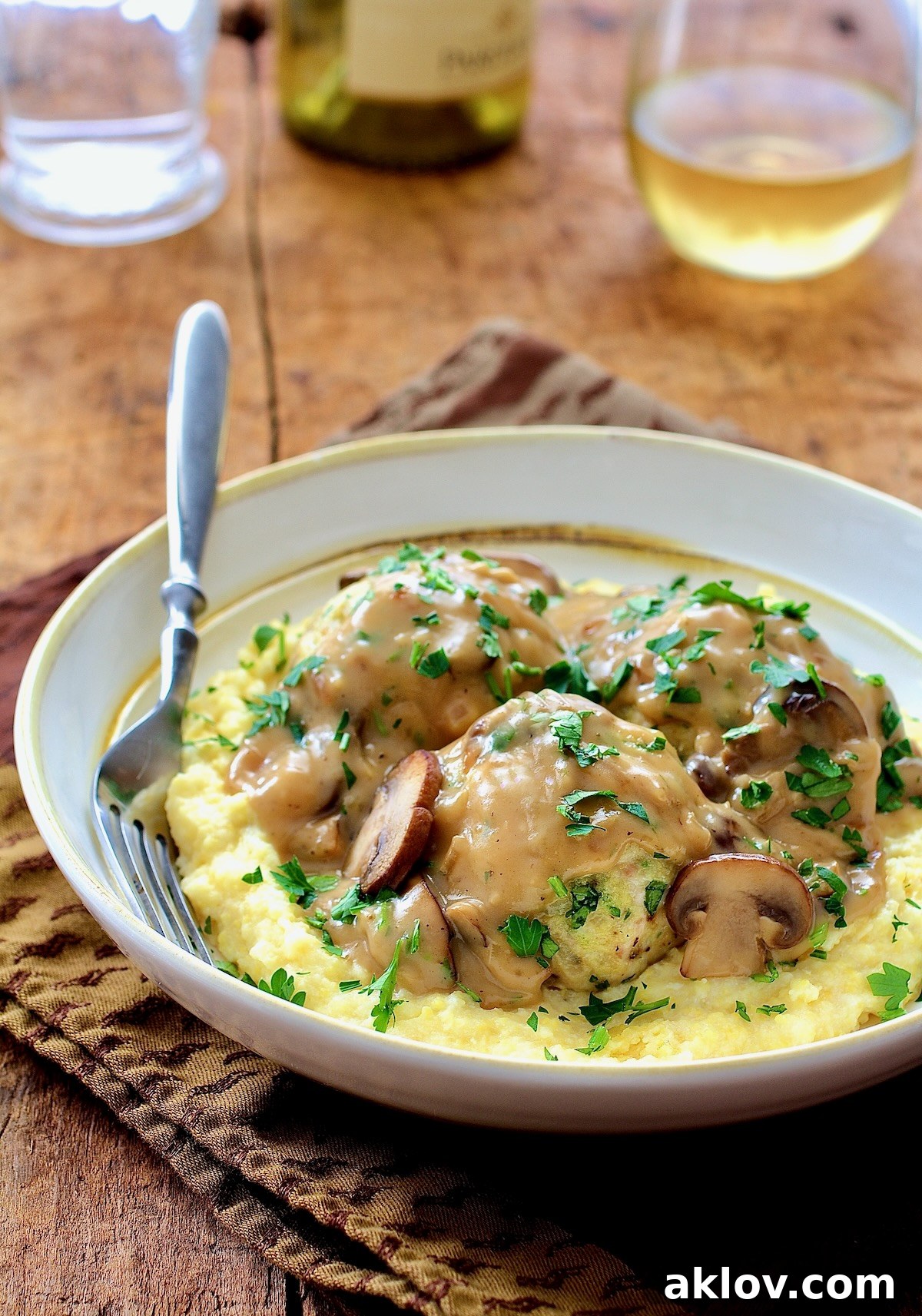 Chicken Marsala Meatballs with Baked Parmesan Polenta, garnished with fresh parsley, served in a white bowl with a fork.