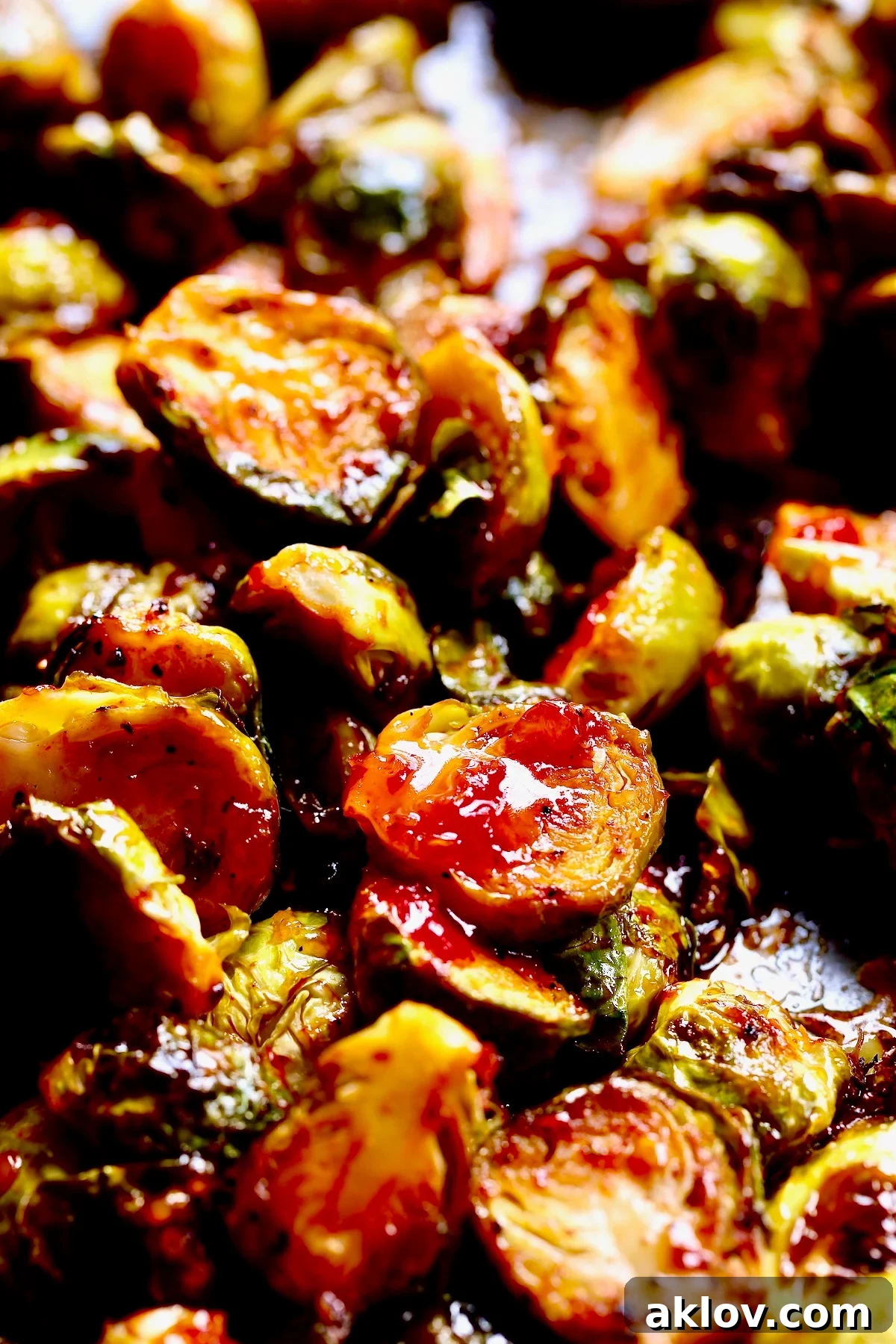 Glazed Sriracha Sweet Chili Brussels Sprouts 11 Roasted Brussels sprouts on a baking sheet, with sweet chili sauce being drizzled over them.