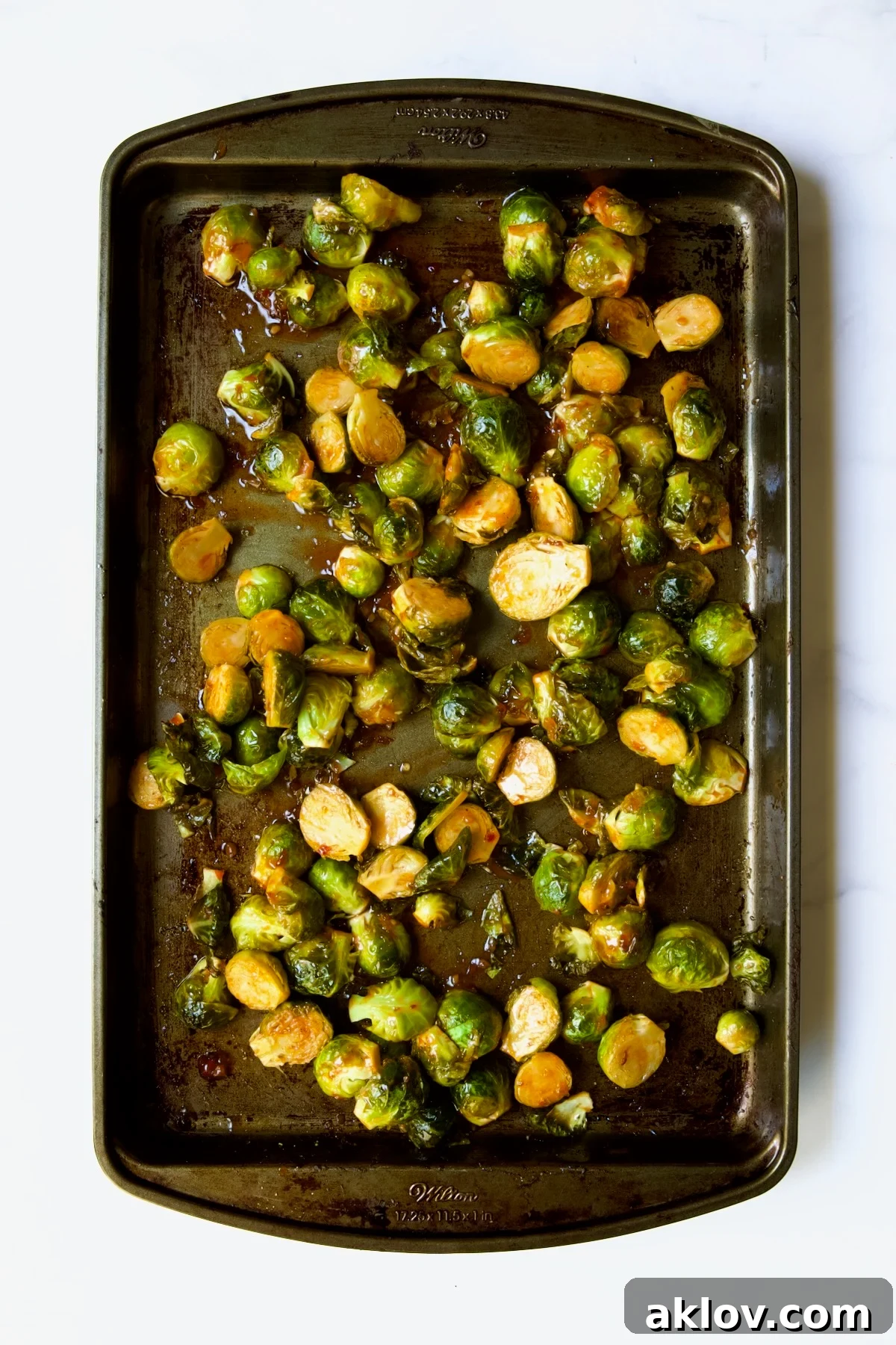 Glazed Sriracha Sweet Chili Brussels Sprouts 12 Roasted Brussels sprouts on a baking sheet, now fully coated and mixed with sweet chili sauce, shimmering and ready to be returned to the oven briefly.