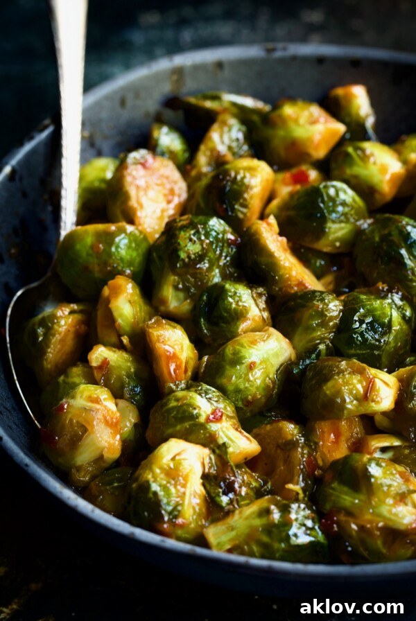 Glazed Sriracha Sweet Chili Brussels Sprouts 15 Sriracha Sweet Chili Roasted Brussels Sprouts in gray speckled bowl with serving spoon.