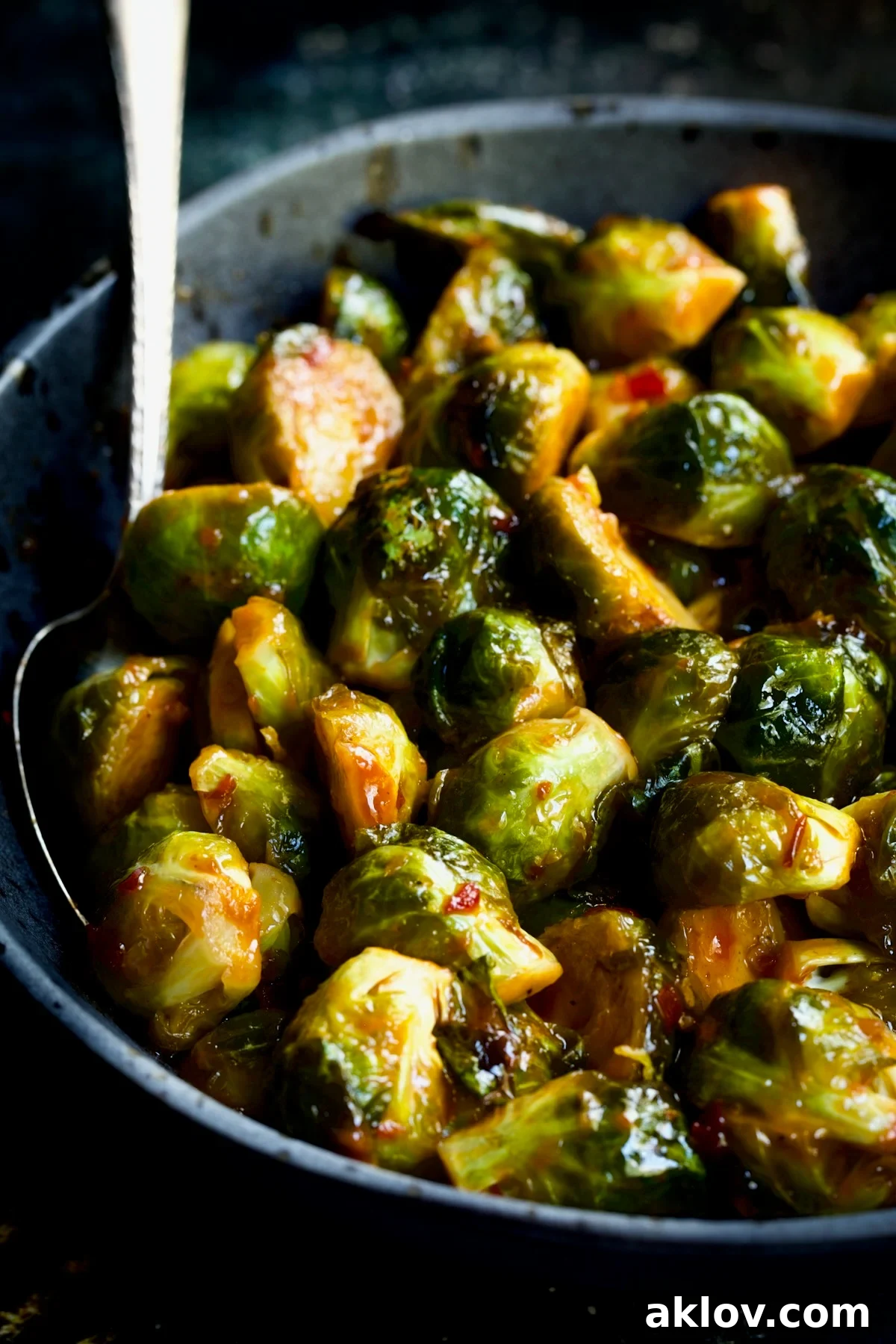 Glazed Sriracha Sweet Chili Brussels Sprouts 3 Sriracha Sweet Chili Roasted Brussels Sprouts in a gray speckled bowl, ready to be served, with a serving spoon tucked into the side.