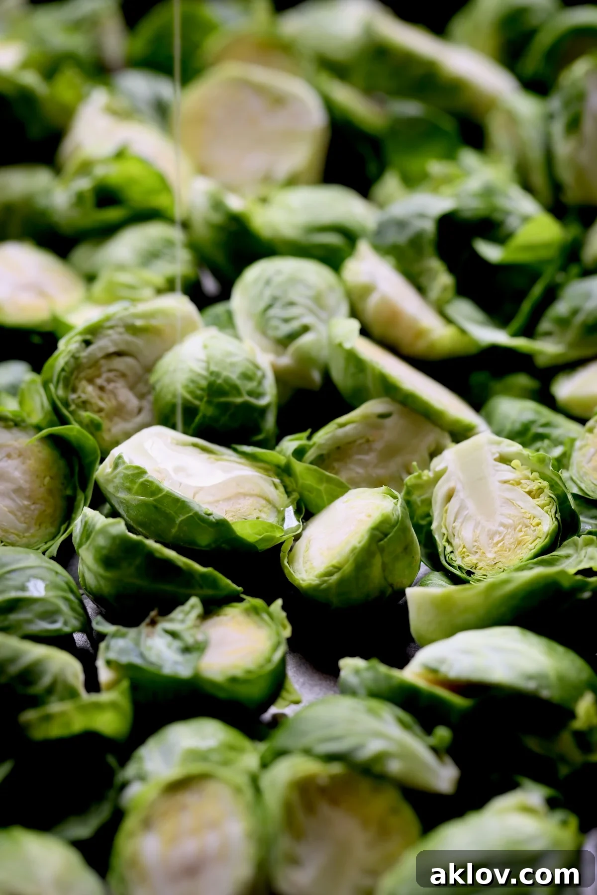 Glazed Sriracha Sweet Chili Brussels Sprouts 6 Halved Brussels sprouts on a baking sheet being drizzled with a neutral oil for roasting.