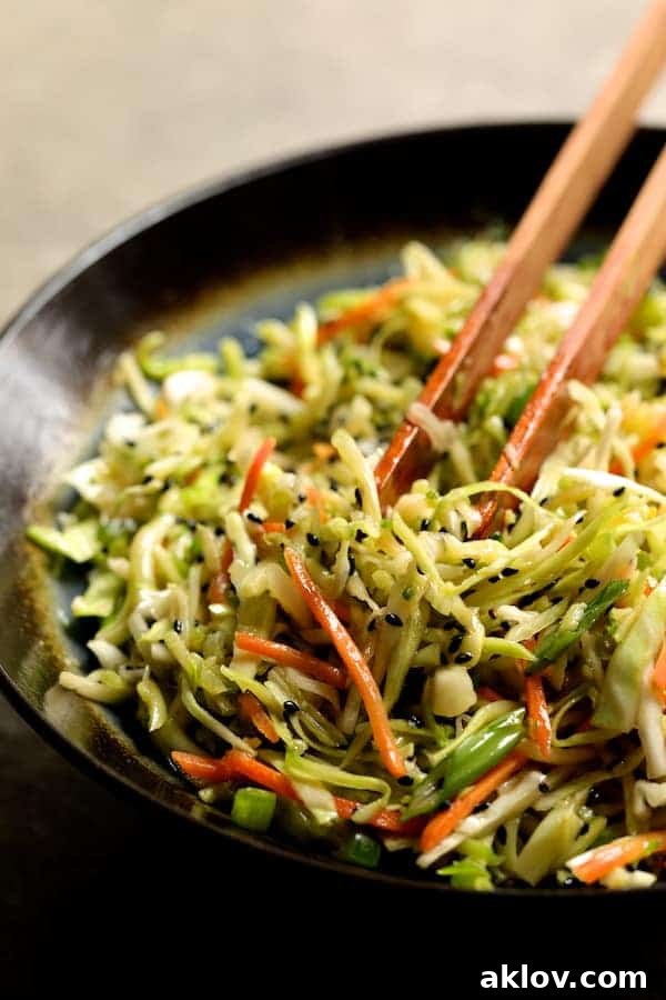 Close-up photo of a vibrant spicy slaw being tossed with tongs in a mixing bowl, showcasing the fresh ingredients.