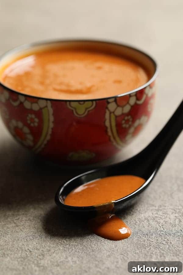 Rich Tahini Gochujang Sauce displayed in a small bowl, with a black spoon holding a dollop of the sauce, highlighting its thick, creamy texture.
