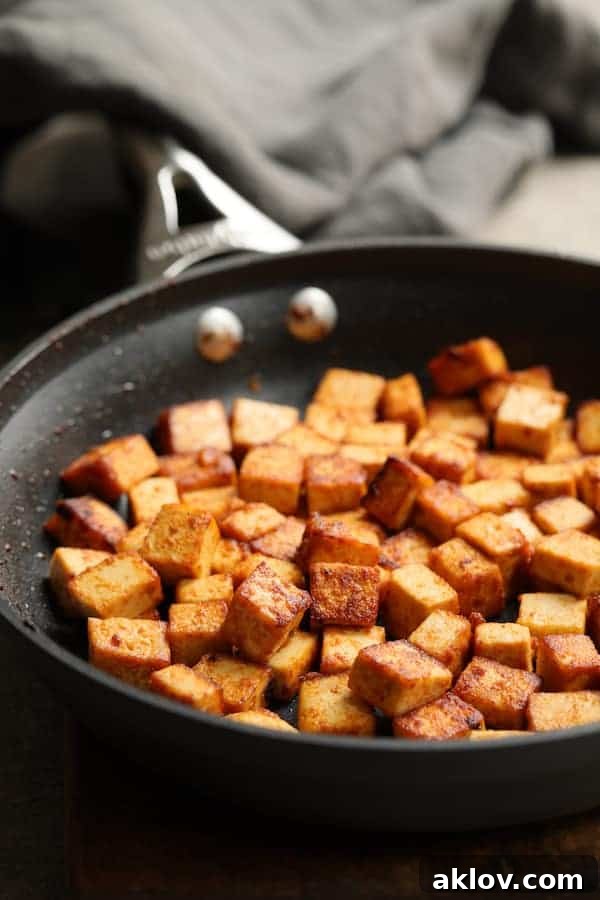 Crispy browned tofu cubes sizzling in a frying pan, coated in a savory sauce, ready to be added to the lettuce wraps.