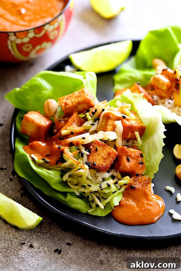 Close-up view of a beautifully assembled Vegan Korean Tofu Lettuce Wrap on a black plate, garnished with lime wedges and sesame seeds.