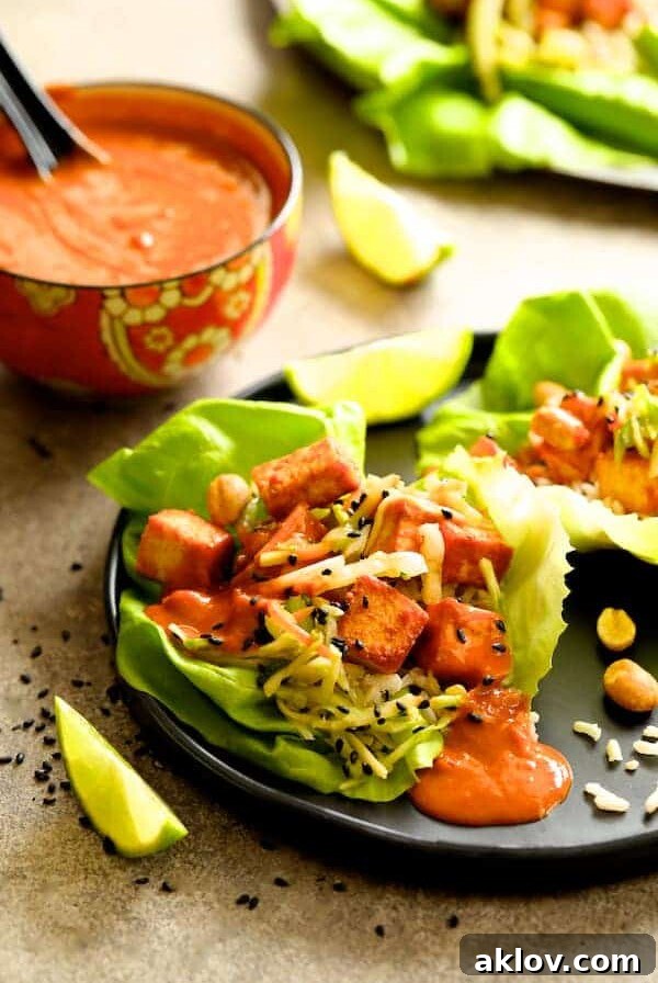 A single Vegan Korean Tofu Lettuce Wrap with Tahini Gochujang Sauce and Spicy Slaw on a black plate, ready to be eaten.