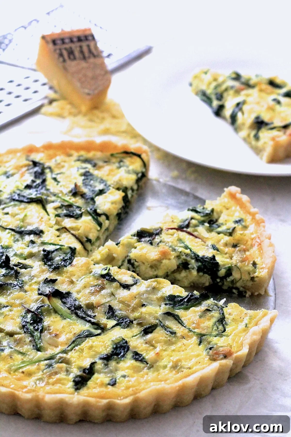 A beautifully baked Leek, Greens, and Gruyere Tart with two slices cut out, showcasing its rich filling and golden crust.