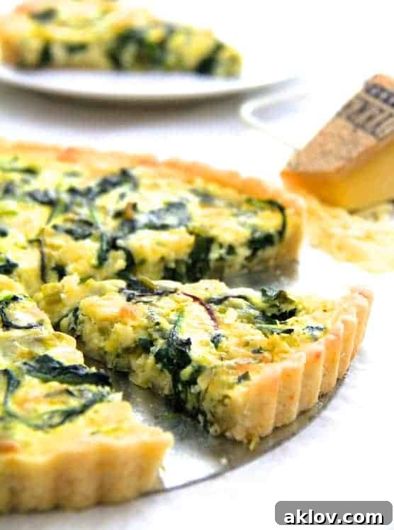 A close-up of a slice of Spring Green, Leek, and Gruyere Tart with scattered shredded cheese in the background.