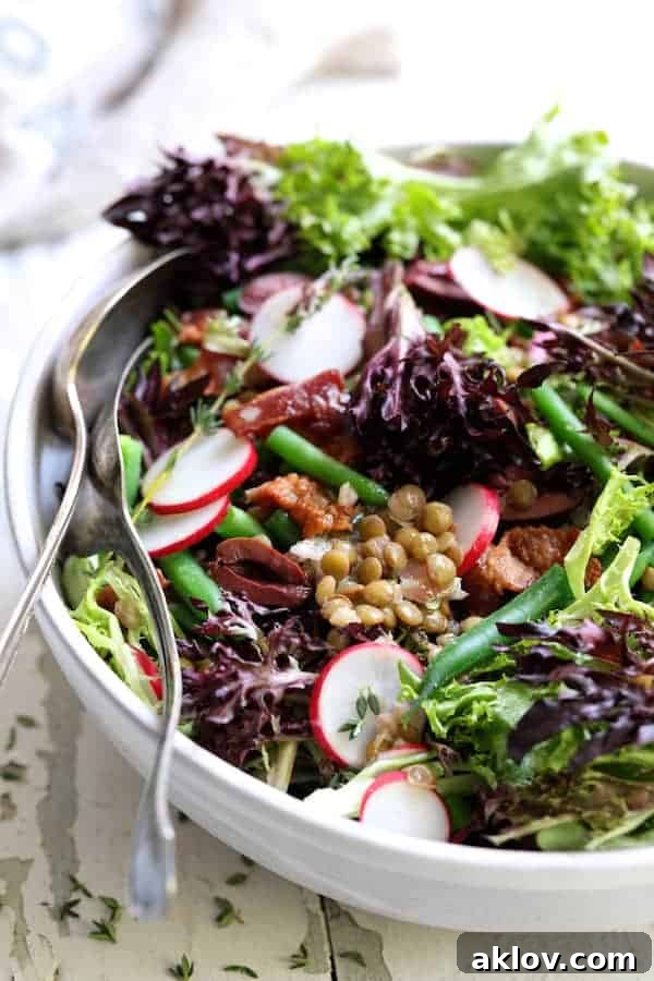 Rustic French Lentil Salad 8 Close-up photo of French Lentil Salad in white bowl on white background with serving spoon and fork.