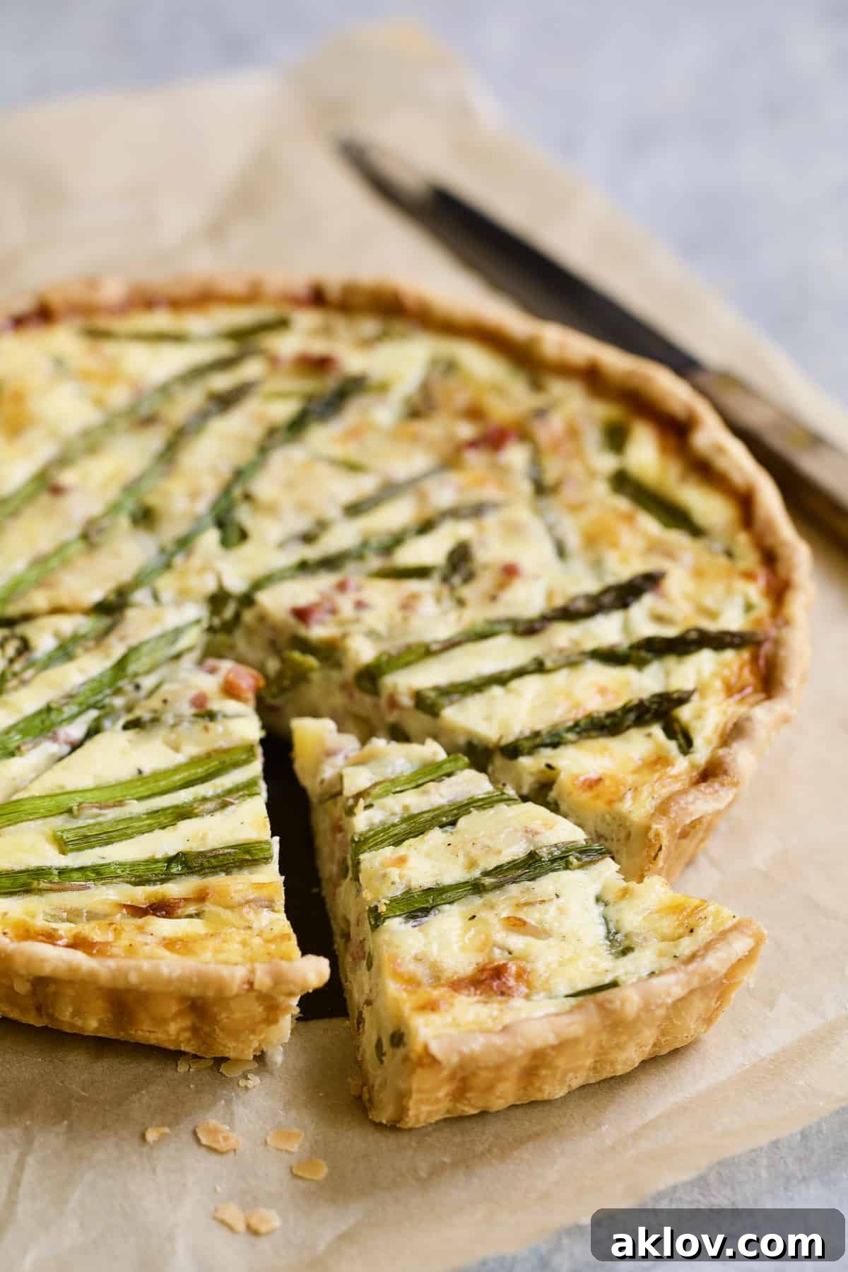 Savory Asparagus Tart with Prosciutto and Fontina 12 Photo of a fully baked Asparagus Prosciutto and Fontina Tart on brown parchment paper, with three wedges already cut and removed, showcasing the golden crust and vibrant filling.