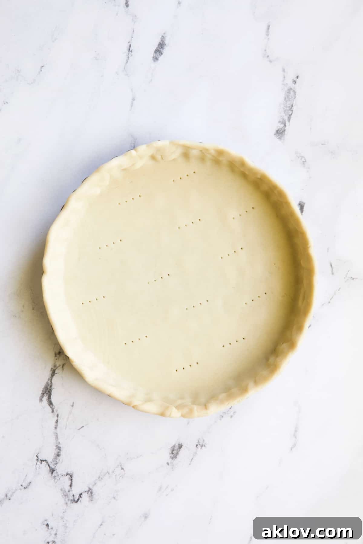 Savory Asparagus Tart with Prosciutto and Fontina 5 Photo of unbaked pie crust docked with a fork, placed in a tart pan on a marble surface, ready for blind baking.