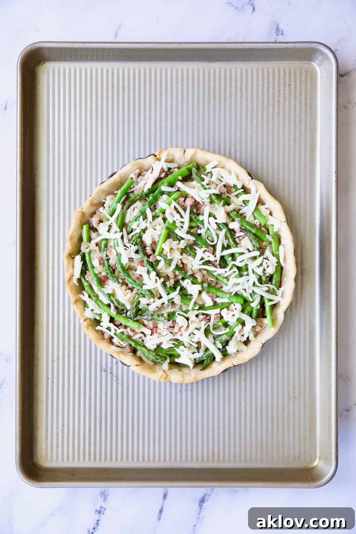 Savory Asparagus Tart with Prosciutto and Fontina 9 Photo of the partially assembled Asparagus Prosciutto and Fontina Tart on a baking sheet, filled with layers of cheese, prosciutto, and asparagus, ready for the custard.