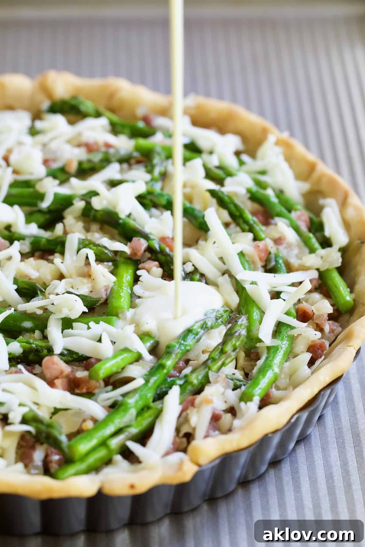 Savory Asparagus Tart with Prosciutto and Fontina 10 Photo of a creamy egg and half-and-half custard being poured over the assembled Asparagus Prosciutto and Fontina Tart filling.