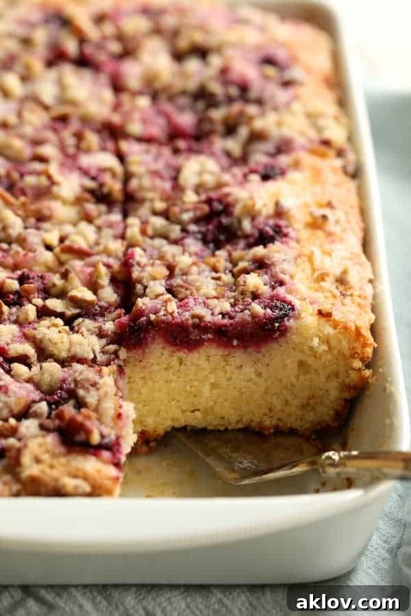 Photo of Easy Raspberry Coffee Cake cut into pieces looking straight on with silver server about to remove a piece.