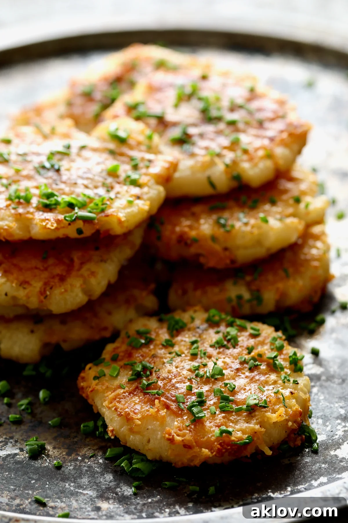 A stack of perfectly golden Parmesan Crusted Crushed Turnips, artfully arranged on a stainless steel tray, highlighting their appealing texture.
