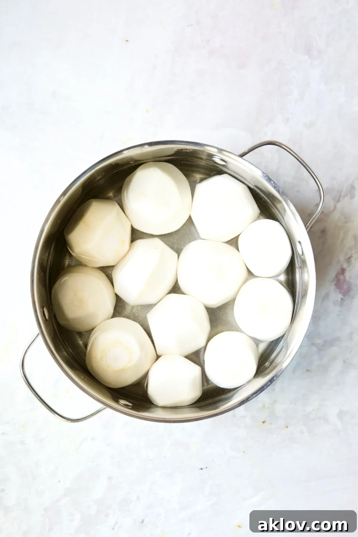 Uncooked, peeled turnips submerged in salted water within a gleaming stainless steel pot, ready for boiling.