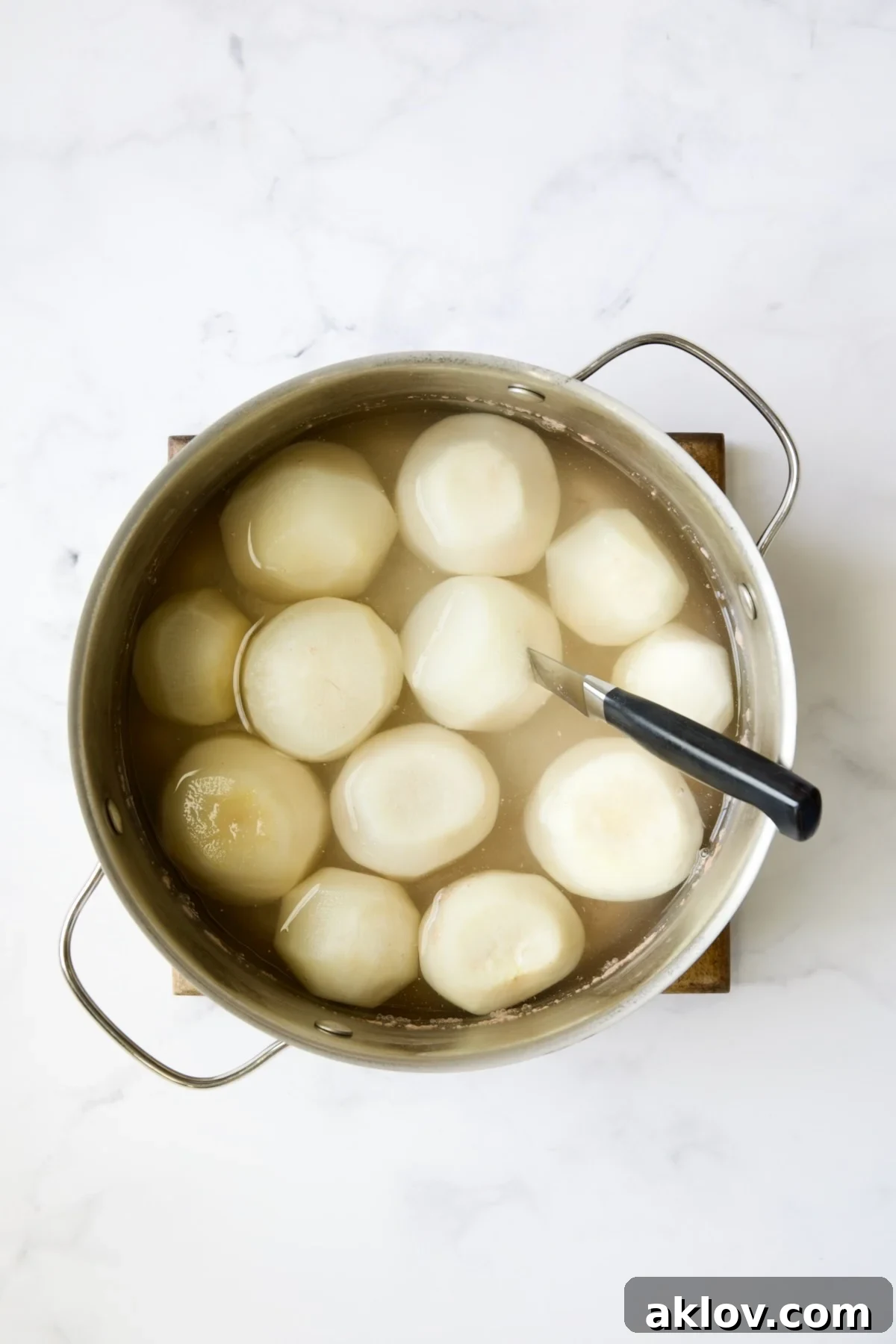 Perfectly cooked turnips resting in a stainless steel pot, with one turnip gently pierced by a paring knife to demonstrate ideal tenderness.