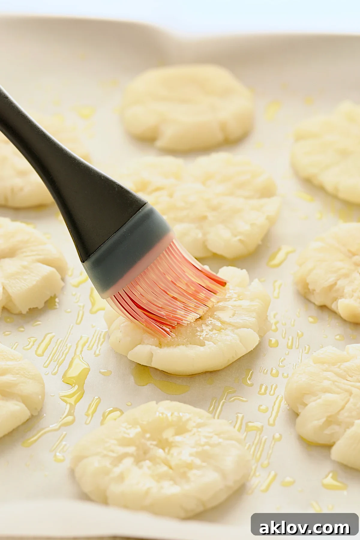 Smashed turnips arranged on parchment paper, being brushed with a savory olive oil and garlic mixture before the Parmesan cheese application.