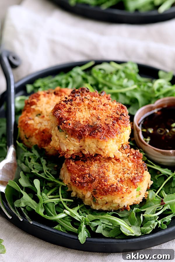 Crispy Tuna Kimchi Cakes with Soy Ginger Dipping Sauce on a black plate, garnished with fresh arugula and a small bowl of dipping sauce.