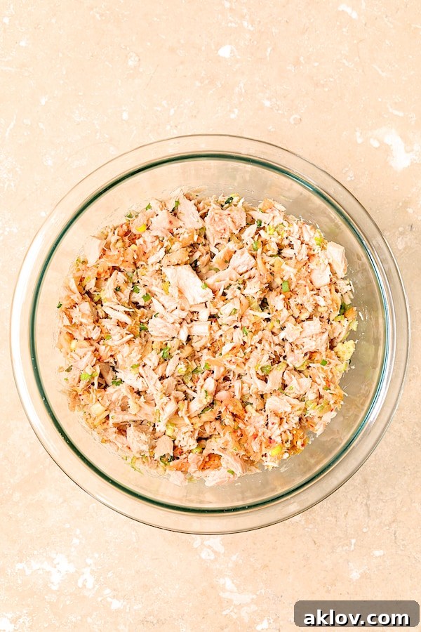Close-up photo of tuna kimchi mixture in a clear glass mixing bowl, showcasing the vibrant ingredients before forming the cakes.