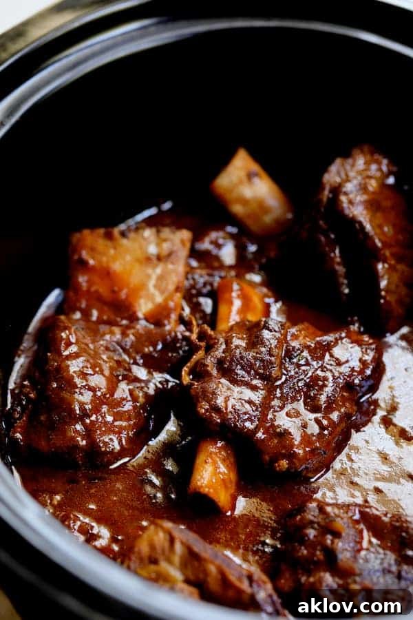 Perfectly cooked beef short ribs simmering in a rich, flavorful barbacoa sauce within a slow cooker.
