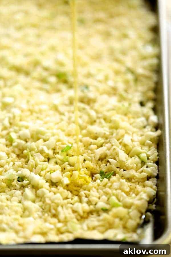 Cauliflower rice being drizzled with olive oil and lime juice on a sheet pan, ready for roasting to perfection.