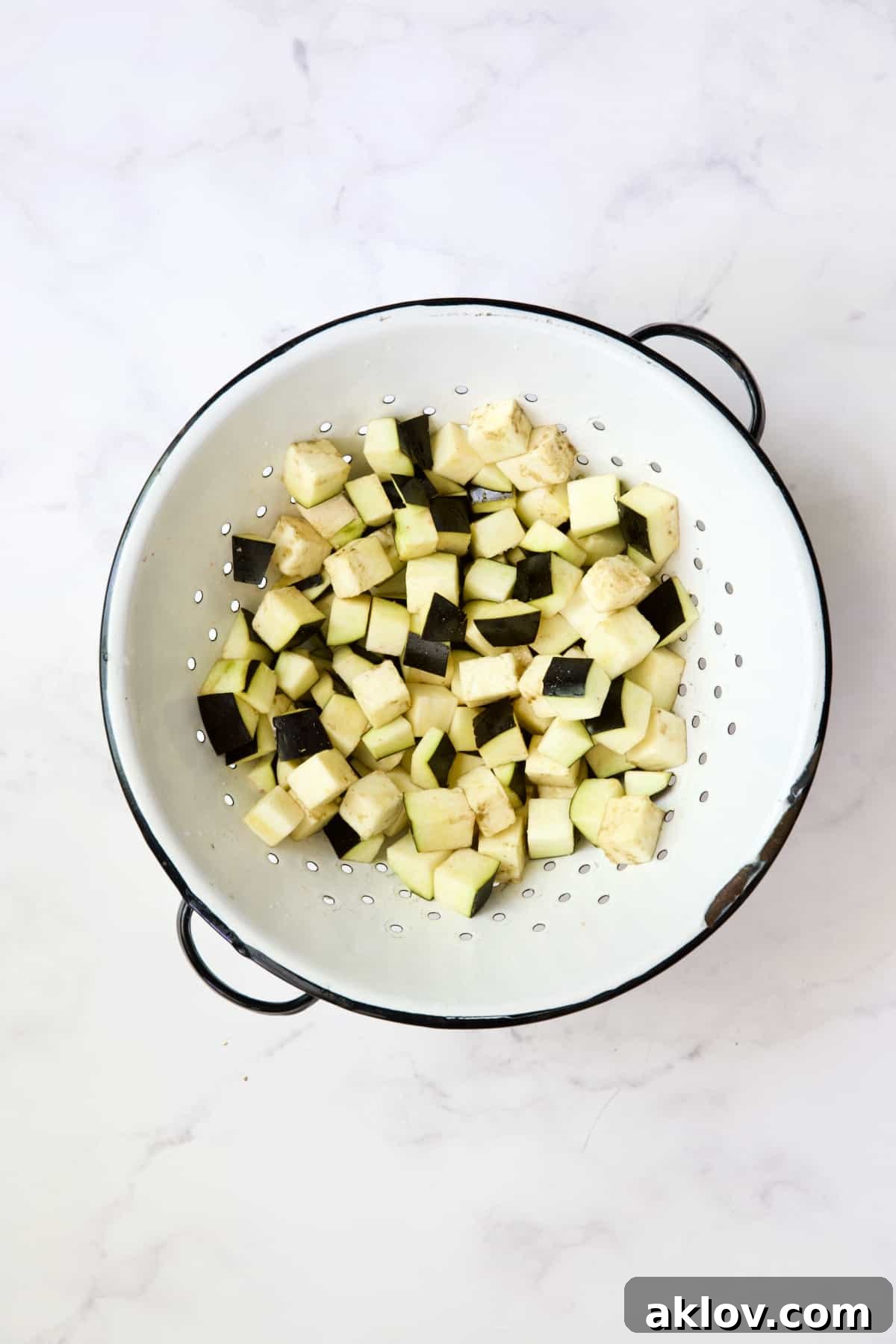Cubed eggplant in white colander.