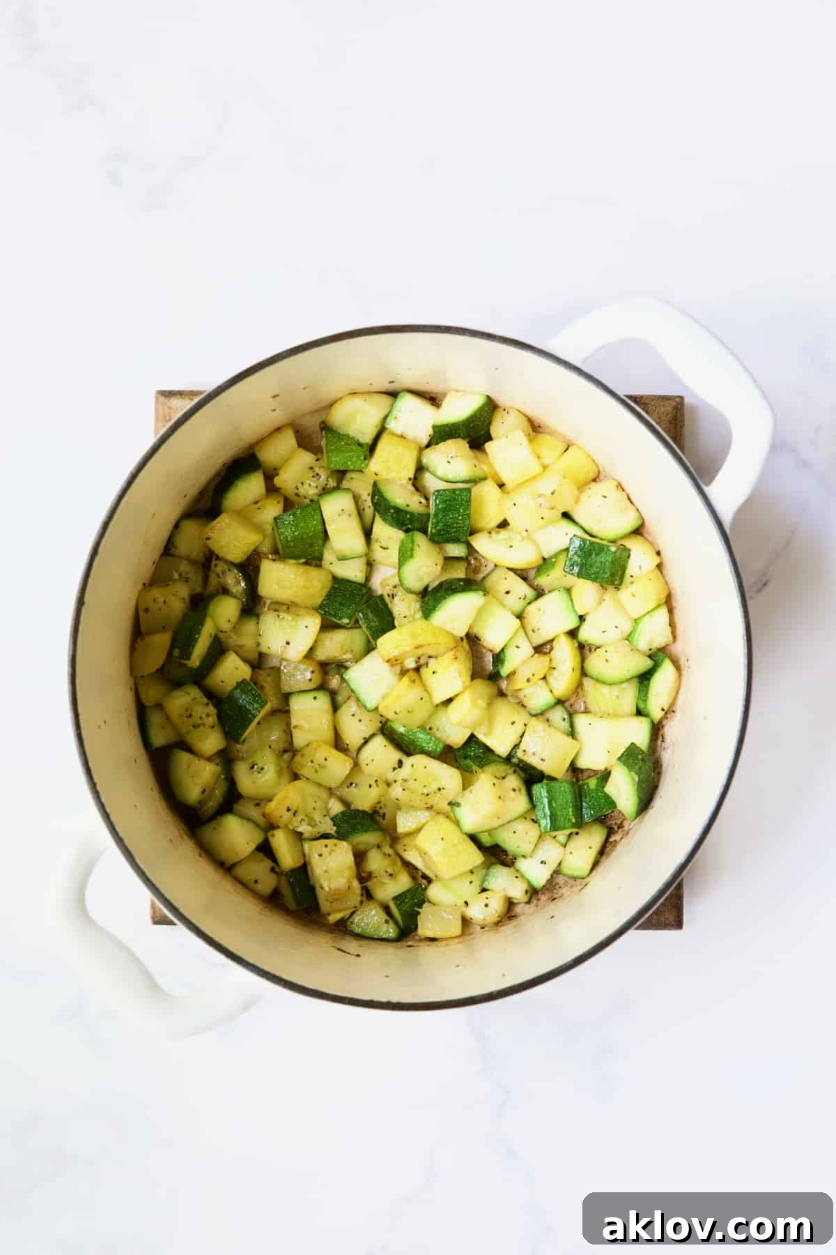 Zucchini and yellow squash being cooked in white Dutch oven.
