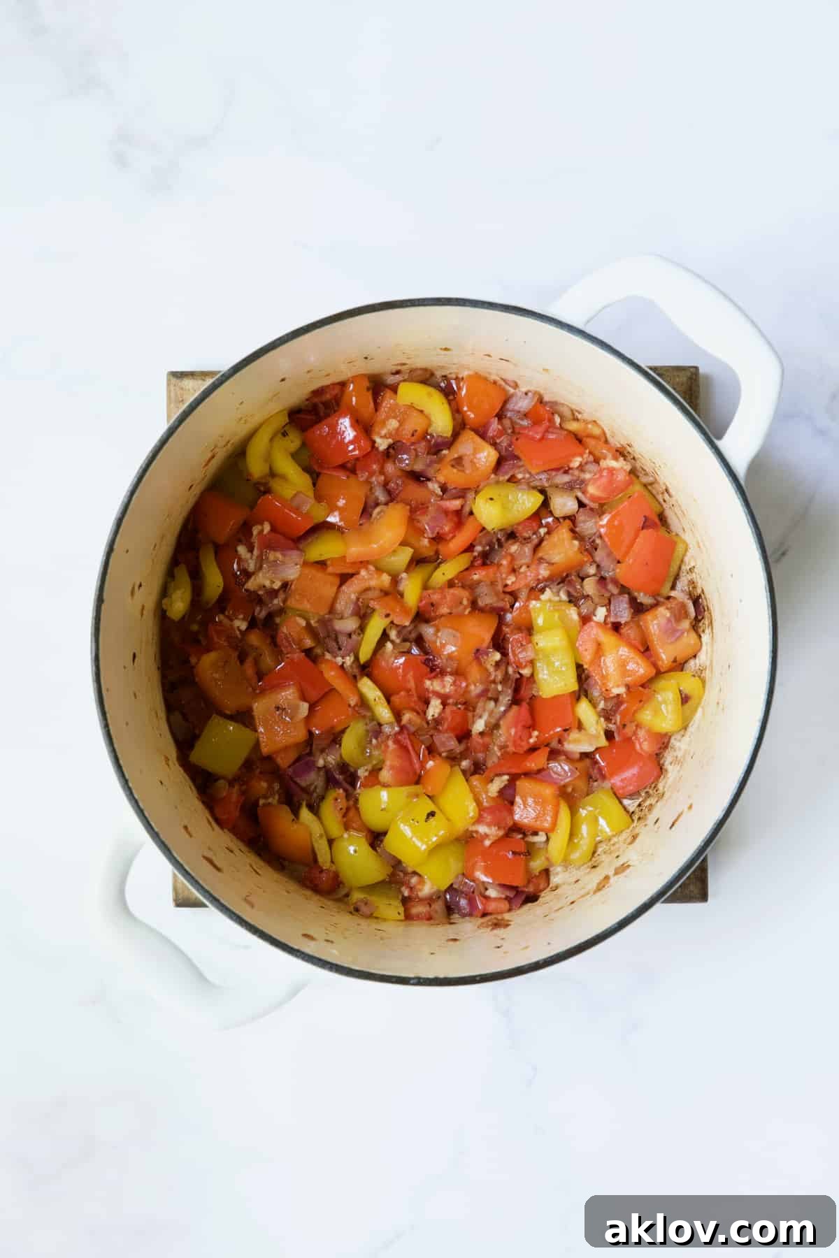 Onions and peppers being cooked in white Dutch oven.