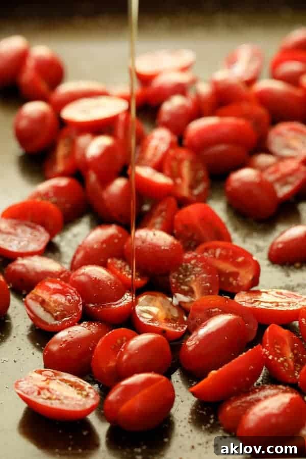 Photo of tomatoes on baking sheet being drizzled with olive oil before being roasted.