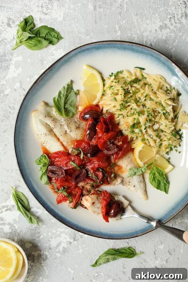 Photo of Baked Fish with Cherry Tomato Olive Sauce and Lemon Chive Asiago Orzo on blue-rimmed plate with a forkful cut from the fish.