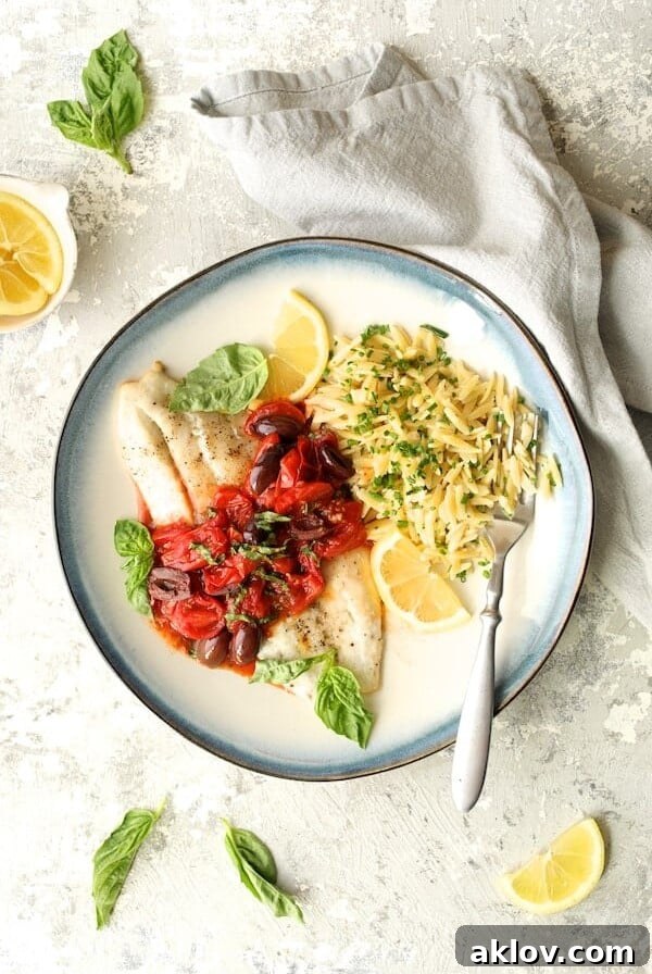 Baked Fish with Cherry Tomato and Olive Sauce and Lemon Chive Asiago Orzo hero shot on blue-rimmed plate