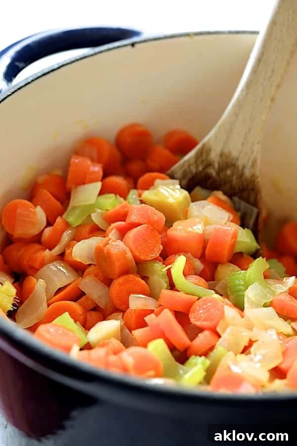 Carrots, onions, celery, ginger, and garlic being sautéed and stirred in a blue Dutch oven, building the soup's flavor base.