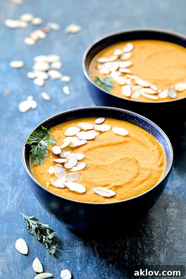 Spicy Indonesian Vegan Carrot Almond Soup served in black bowls, garnished with sliced almonds and fresh carrot fronds, presented on a blue background.