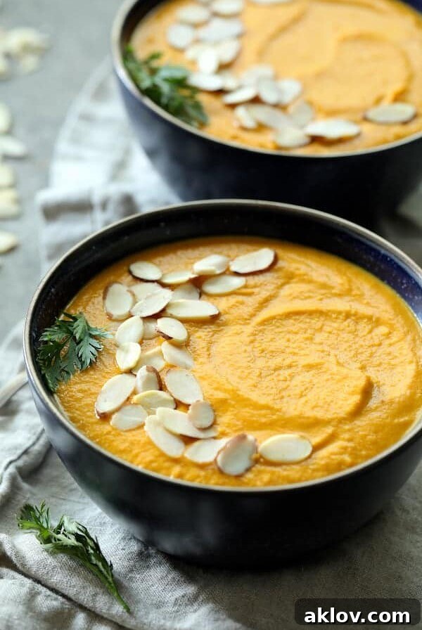 Spicy Indonesian Vegan Carrot Almond Soup closeup garnished with a carrot top sprig and sliced almonds.