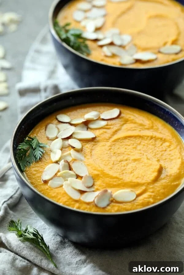 Spicy Indonesian Vegan Carrot Almond Soup closeup, garnished with a carrot top sprig and sliced almonds.