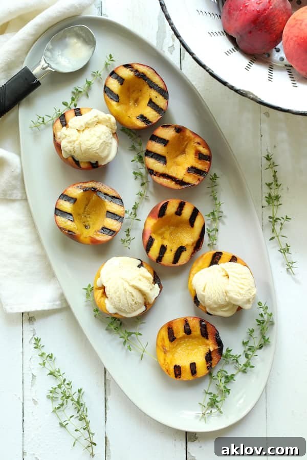 Photo of grilled peaches on white oval platter with ice cream added to three of the peaches.