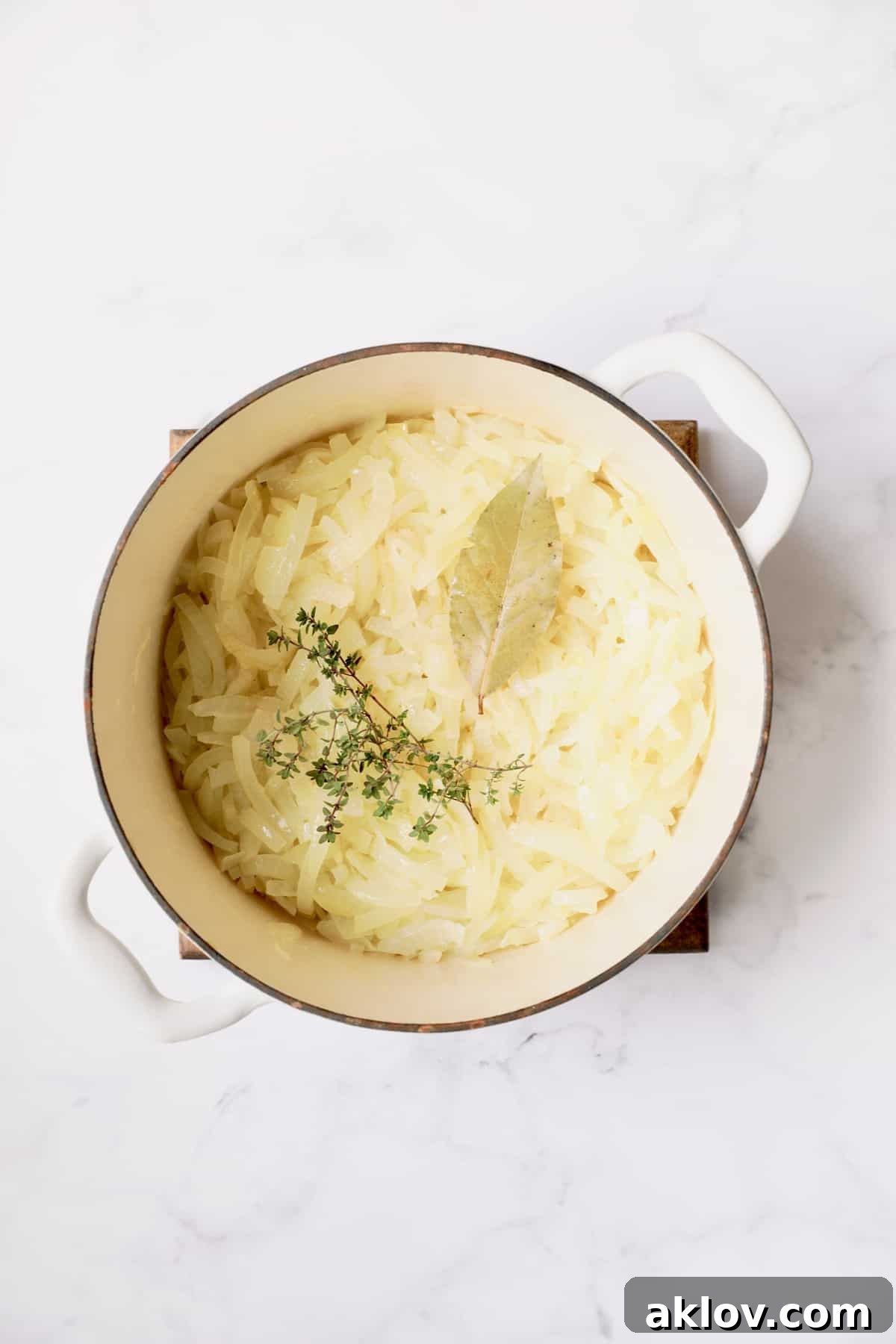 Date Night French Onion Indulgence 6 Photo of partially cooked onions with thyme and bay leaf in white Dutch oven.