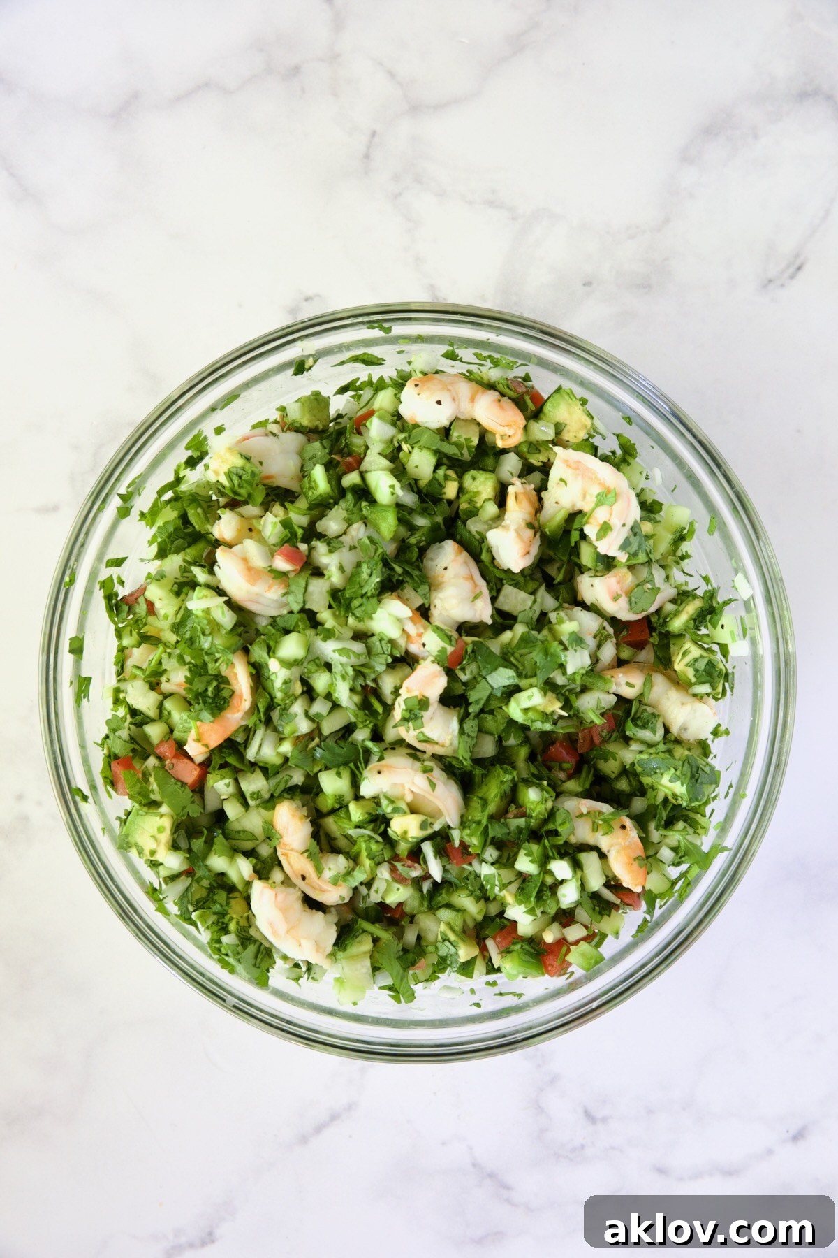 Shrimp added to vegetables in glass bowl.