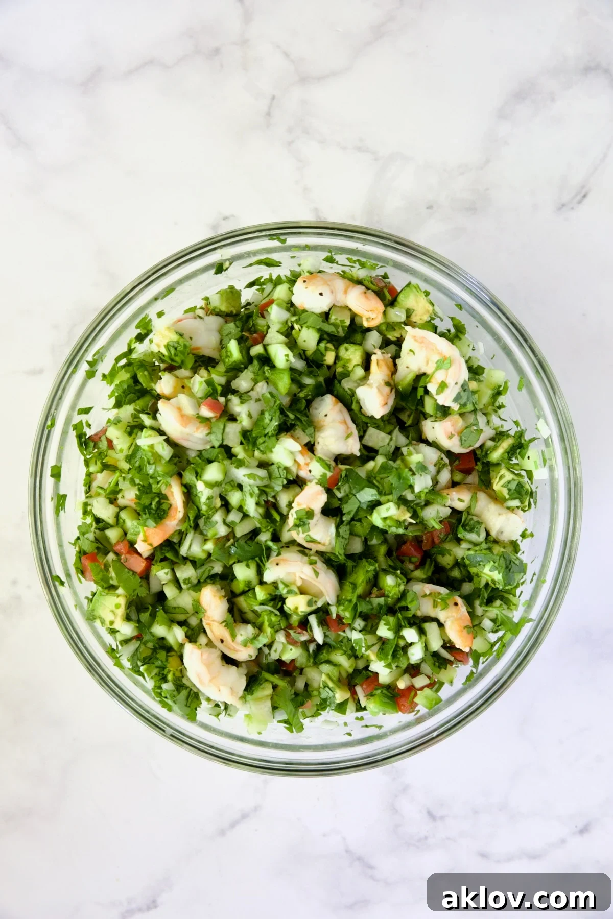 Cooked shrimp thoughtfully added to the vibrant vegetable mixture in a large glass bowl.