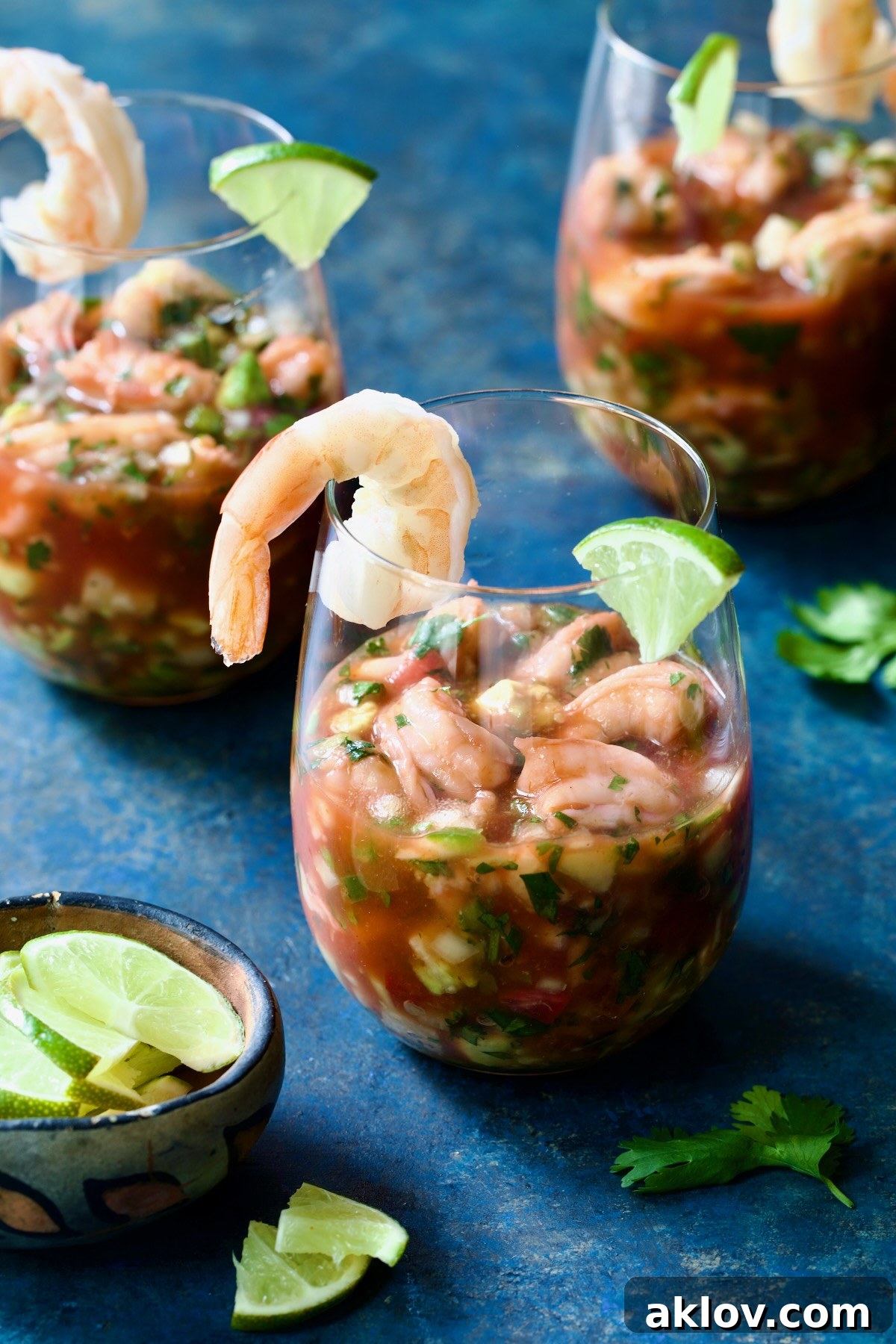 Three glasses of Mexican Shrimp Cocktail garnished with lime wedges.