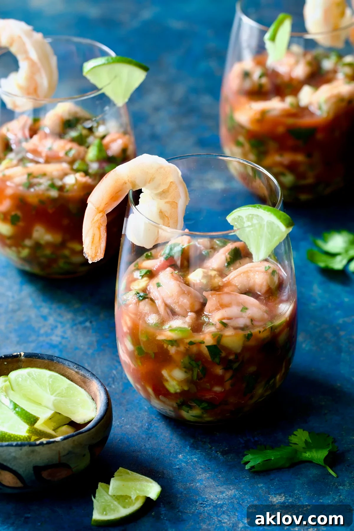Three elegant glasses of Mexican Shrimp Cocktail, garnished with lime wedges and cilantro sprigs, ready to be served.